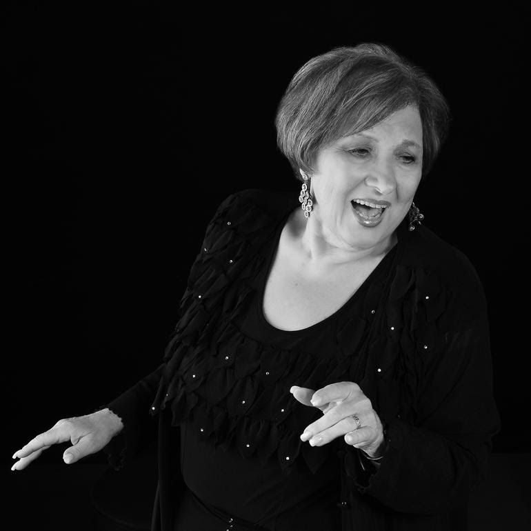 A black and white photo of a woman in an evening gown and earrings, singing and swaying her arms