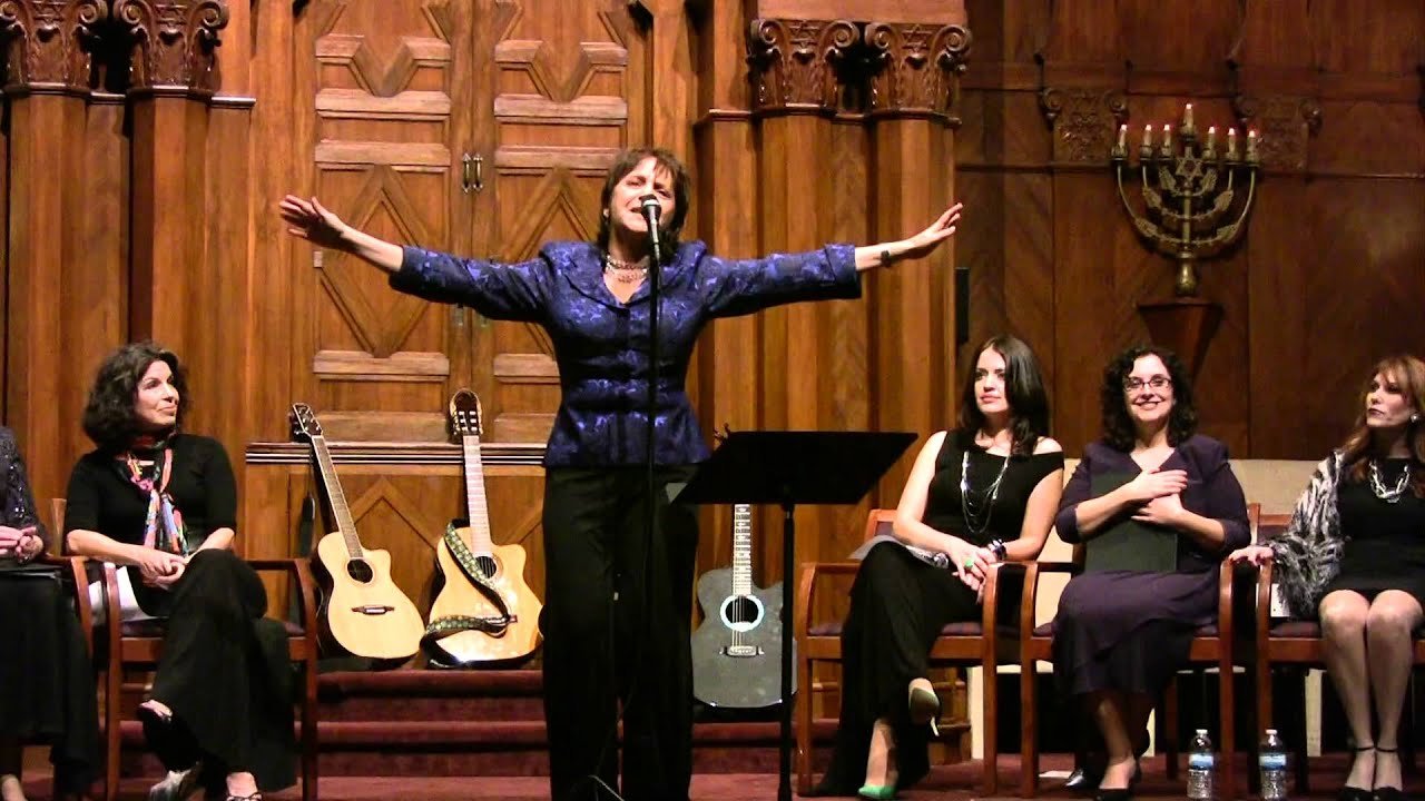 Alejandra Czarny sings with outstretched arms, 4 people sit and listen