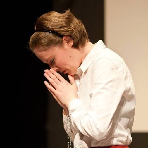 a person with a headband, in a white shirt and red skirt praying with a rosary