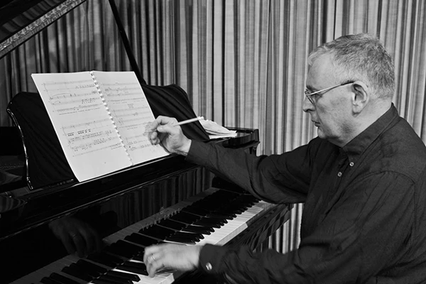 a black and white photo of Daniel Galay, playing the keys with his left hand and writing notes with his right