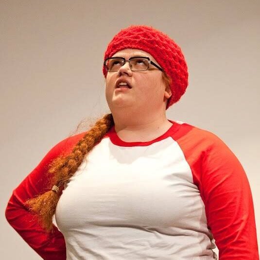 a person with a braid, in a red hat and red and white shirt, looking up, with arm at hip