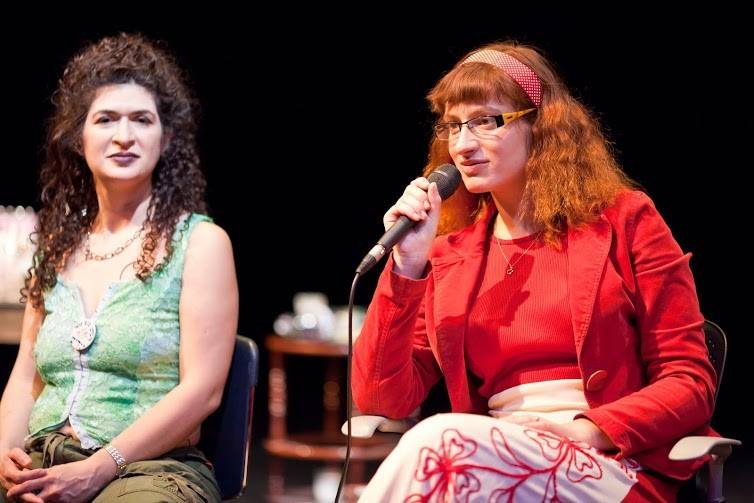 jana Mazurkiewicz Meisarosh speaking into a microphone, Sara Feldman sits