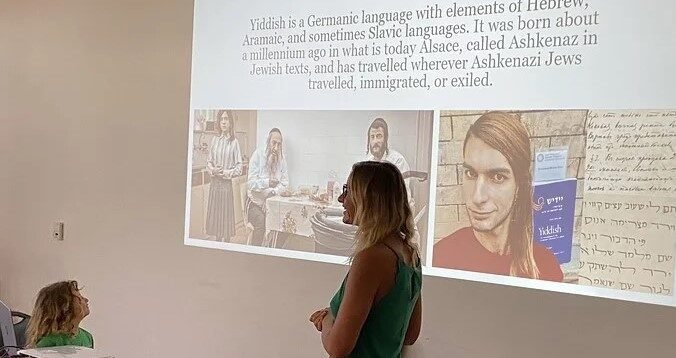 Jana Mazurkiewicz Meisarosh presenting, and Esterke is looking on. the slideshow reads "what is yiddish?"